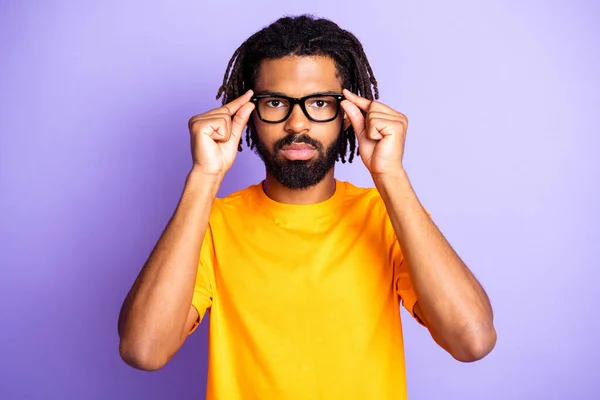 Porträtt av fina allvarliga brunett frisyr kille touch glasögon bära orange t-shirt isolerad på syren färg bakgrund — Stockfoto