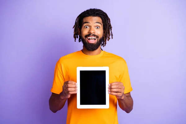 Foto de optimista agradable morena hombre mantenga tableta llevar camiseta amarilla aislada sobre fondo de color púrpura —  Fotos de Stock
