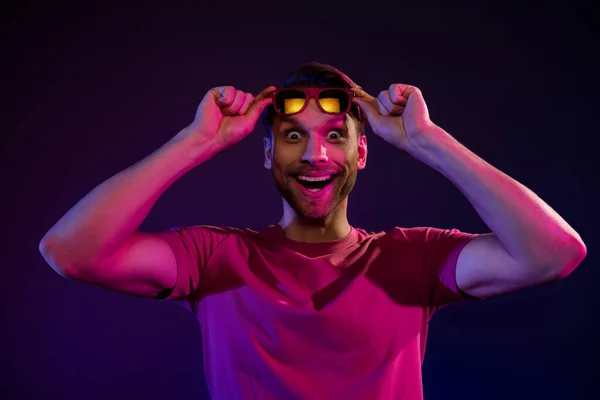 Portret van aantrekkelijke vrolijke verbaasd man aanraken specs plotselinge nieuws reactie geïsoleerd over donker neon paarse kleur achtergrond — Stockfoto