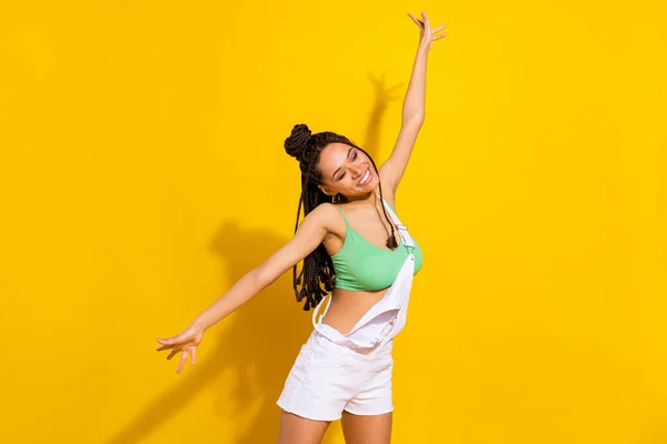 Foto de adorável brilhante mulher de pele escura vestida branco geral dança braços lados sorrindo isolado cor amarela fundo — Fotografia de Stock