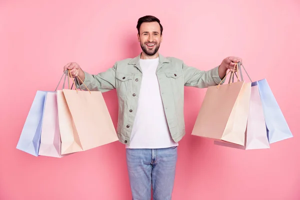 Retrato de atractivo alegre chico sosteniendo en bolsas de manos presenta fin de semana aislado sobre fondo de color pastel rosa —  Fotos de Stock