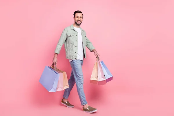 Вид в полный рост на привлекательного веселого парня, идущего с подарками, выделяется на розовом фоне. — стоковое фото