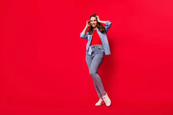 Foto de dulce adorable joven mujer usar jeans camisa sonriente brazos pelo buscando espacio vacío aislado color rojo fondo — Foto de Stock