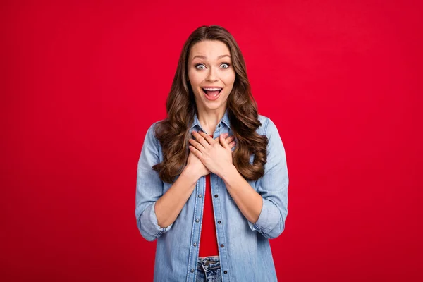 Foto de encantadora mujer joven impresionada usar jeans camisa brazos sonrientes pecho boca abierta aislado color rojo fondo — Foto de Stock