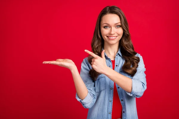 Retrato de menina alegre atraente segurando na palma demonstrando anúncio espaço cópia isolado sobre fundo de cor vermelha vibrante — Fotografia de Stock