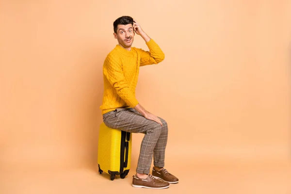 Foto retrato visão de corpo inteiro do homem sentado na mala arranhando cabeça isolada no fundo de cor bege pastel — Fotografia de Stock