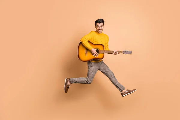Retrato fotográfico completo de un tipo tocando la guitarra saltando aislado sobre fondo de color beige pastel —  Fotos de Stock