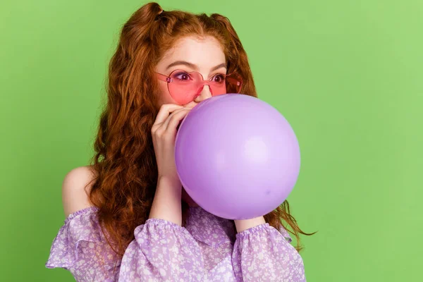 Foto de penteado vermelho doce jovem senhora sopro balão olhar espaço vazio desgaste violeta blusa óculos isolados no fundo cor verde — Fotografia de Stock