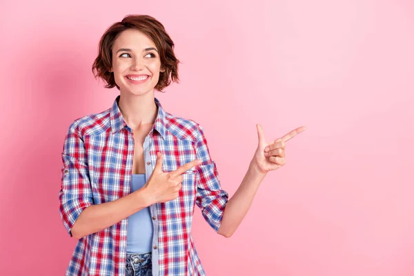 Photo of shine beaming young lady dressed plaid shirt pointing looking empty space isolated pink color background — Stock Photo, Image