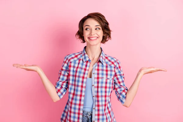 Φωτογραφία από χαριτωμένο γλυκό νεαρή γυναίκα φορούν καρό πουκάμισο προτείνοντας να επιλέξετε το προϊόν ψάχνει κενό χώρο απομονωμένο ροζ χρώμα φόντο — Φωτογραφία Αρχείου
