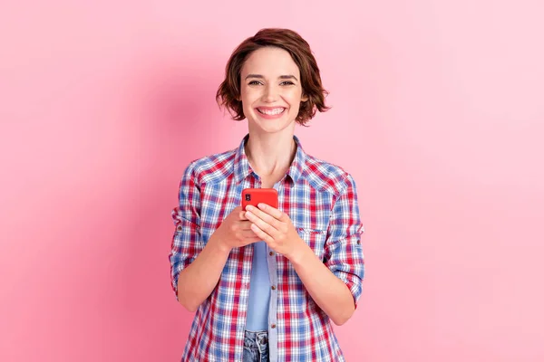 Foto de linda joven dama vestida camisa a cuadros sosteniendo brazos dispositivo moderno aislado color rosa fondo — Foto de Stock
