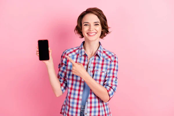 Фото очаровательной милой юной леди, одетой в клетчатую рубашку, указывающую на руки современным устройством, изолированным розовым цветом фона — стоковое фото