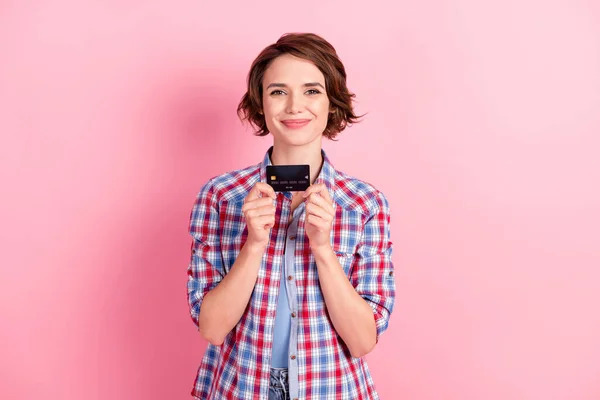Foto de encantadora joven brillante vestido camisa a cuadros sosteniendo brazos manos tarjeta de crédito aislado color rosa fondo —  Fotos de Stock