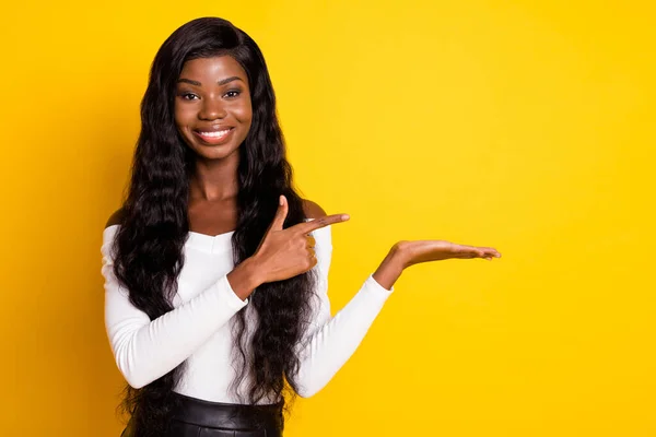 Foto de morena afro-americana jovem segurar mão apontar espaço vazio dedo isolado no fundo de cor amarela — Fotografia de Stock