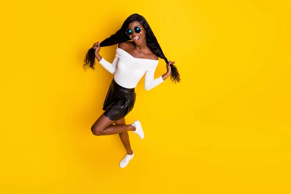 Visão de alto ângulo na mulher de pele preta alegre fazendo caudas com roupa elegante de cabelo longo isolado no fundo de cor amarela vibrante — Fotografia de Stock