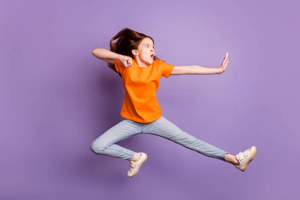 Foto de perfil de cuerpo completo de jengibre óptimo niña salto usar pantalones vaqueros camiseta naranja aislados sobre fondo púrpura —  Fotos de Stock