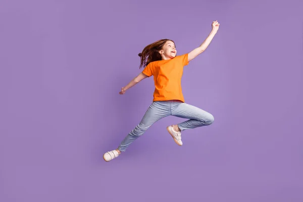 Вид в полный рост на довольно веселую девочку доподросткового возраста, прыгающую на фоне фиолетового цвета — стоковое фото
