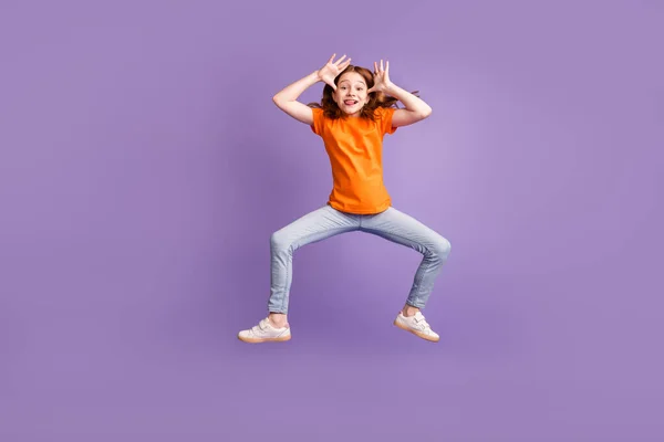 점프하는 생강 머리 소녀의 나체 사진은 보라색 배경에 고립된 티셔츠 청바지를 입고 놀고 있다 — 스톡 사진