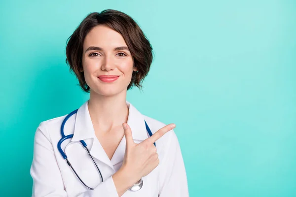 Zdjęcie młodej kobiety lekarz szczęśliwy pozytywny uśmiech wskazują palcem pustej przestrzeni i porad kliniki odizolowane na tle ciemnego koloru — Zdjęcie stockowe