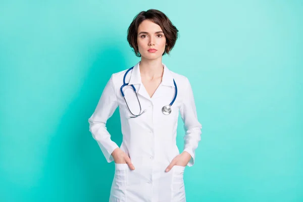 Foto de mujer joven médico terapeuta confiado serio manos en el bolsillo aislado sobre fondo de color verde azulado — Foto de Stock