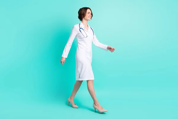 全身型侧貌全身型照片女医生身穿白色制服走在前面，微笑着孤立明亮的茶色背景 — 图库照片