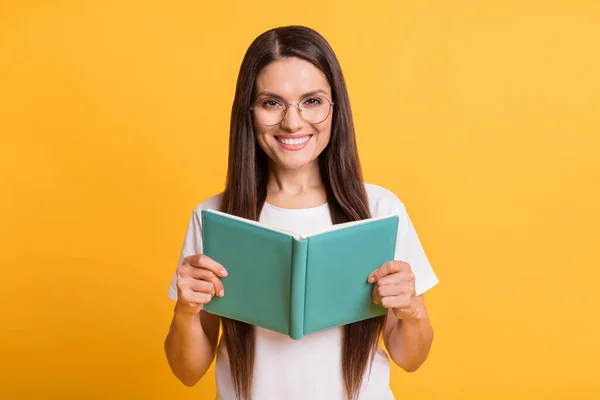 Foto de encantadora mulher madura positiva segurar livro usar óculos t-shirt branca isolada no fundo de cor amarela — Fotografia de Stock