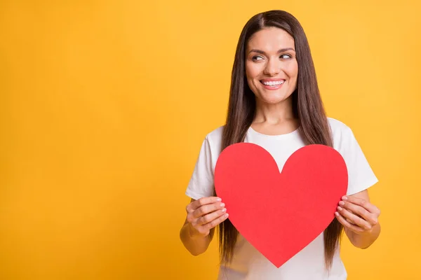 Foto retrato de mulher curiosa segurando papel vermelho coração amor sinal olhando copyspace isolado no fundo de cor amarelo vívido — Fotografia de Stock