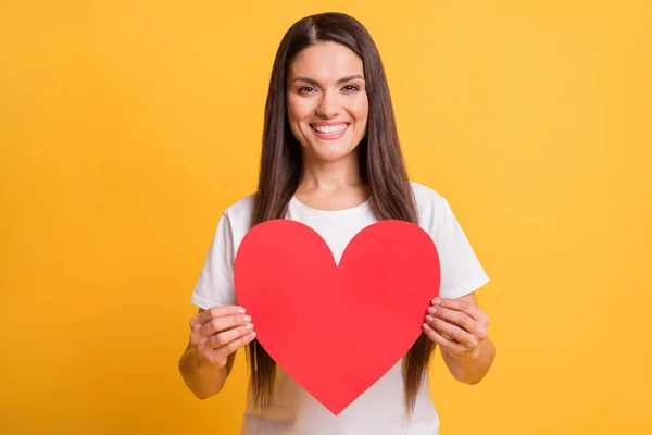Foto retrato de mulher sorridente feliz demonstrando papel vermelho cartão postal coração isolado no fundo cor amarela vibrante — Fotografia de Stock