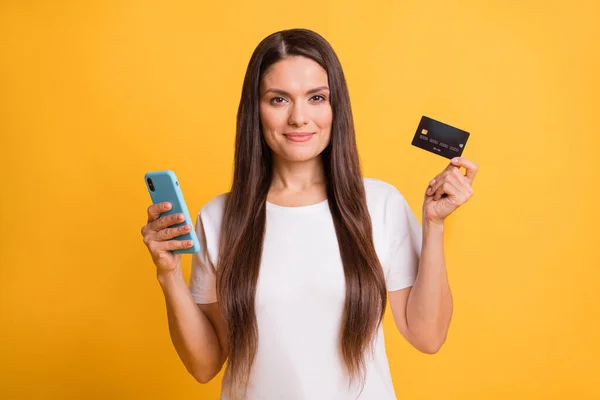 Photo portrait of beautiful latin woman using cellphone holding credit bank card isolated on bright yellow color background — Stock Photo, Image