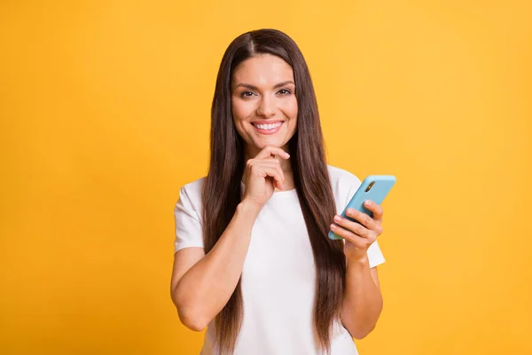 Foto retrato de mujer inteligente reflexiva sonriendo usando el mensaje de escritura del teléfono móvil aislado en un fondo de color amarillo vivo — Foto de Stock