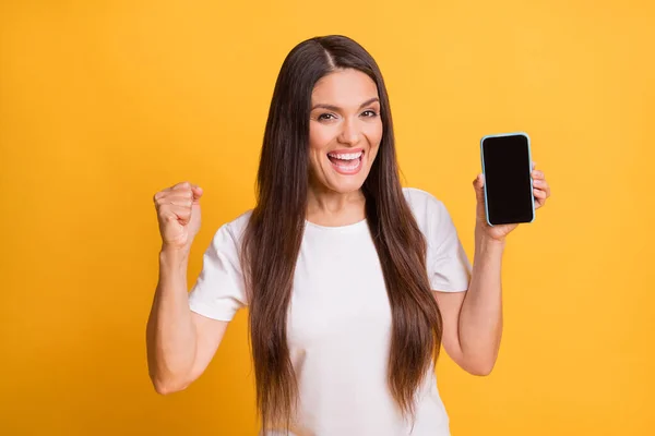 Foto portrét ženy zobrazující dotykový displej smartphone s copyspace gestikuluje jako vítěz izolované na jasně žlutém pozadí — Stock fotografie