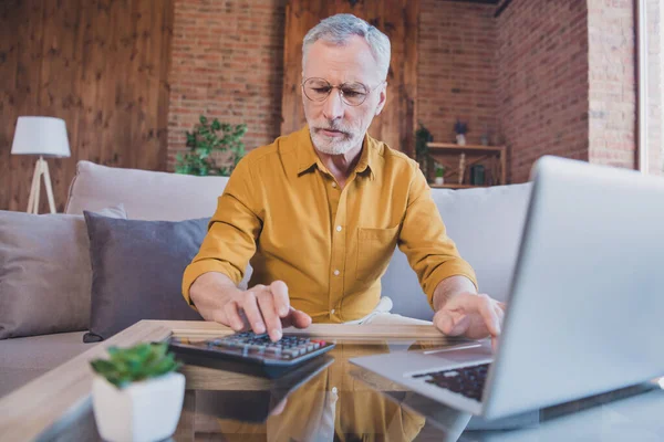 Foto van strenge oudere witte haar man werk laptop zitten dragen bril geel shirt alleen thuis — Stockfoto