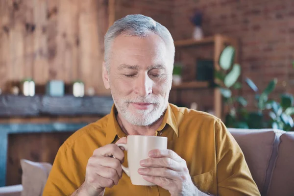 ポジティブな高齢者の写真ソファの腕の上に座ってコーヒーを保持目を閉じ臭い良い気分が屋内 — ストック写真
