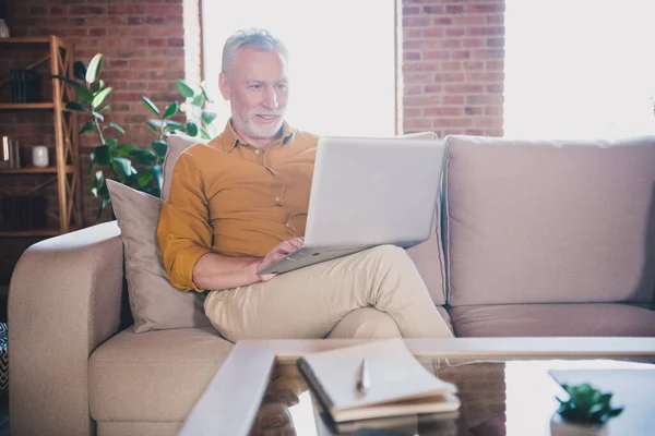 Foto van positieve man zitten op bank hold look laptop tand glimlach hebben goed humeur werken vanuit huis binnen — Stockfoto