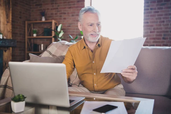 Photo of cheerful person sit on couch look arm hold paper document reading toothy smile have good mood indoors — Stock Photo, Image