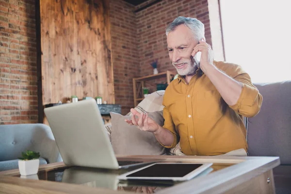 Foto de pessoa bonito positivo sentar no sofá falar telefone olhar laptop ocupado trabalhando de casa dentro de casa — Fotografia de Stock