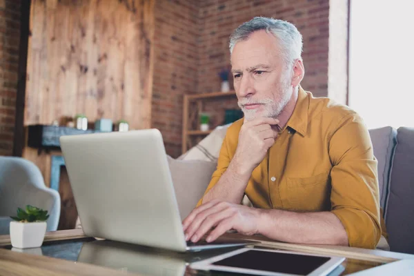 Portret van serieuze bedachtzame oude man zitten op de bank arm op kin kijken geïnteresseerd laptop ponder oplossing thuis — Stockfoto