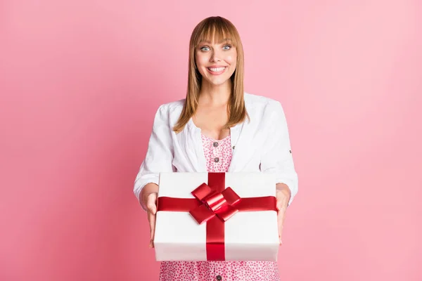 Foto portrét mladá dívka na sobě tištěné šaty dává příjem narozeninová dárková krabice zabalená stuha izolované na pastelové růžové pozadí — Stock fotografie