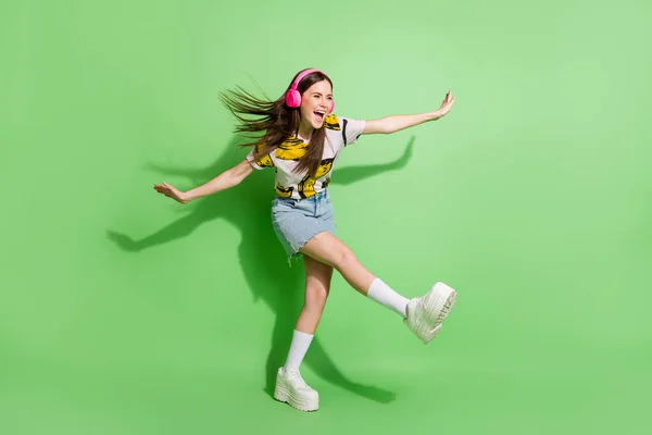 Ganzkörperfoto der brünetten verträumten jungen Frau sehen leer Raum Hände Flügel Tanz tragen Kopfhörer isoliert auf grünem Hintergrund — Stockfoto