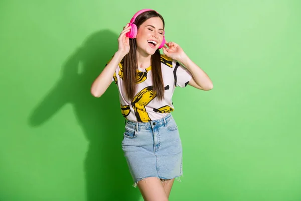 Foto de feliz alegre sonrisa encantadora chica en auriculares disfrutando de la música bailando aislado sobre fondo de color verde — Foto de Stock