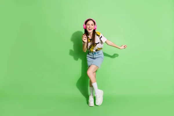 Full length φωτογραφία της χαρούμενης νεαρής γυναίκας χορό καλή διάθεση φορούν ακουστικά απομονώνονται σε πράσινο φόντο χρώμα — Φωτογραφία Αρχείου