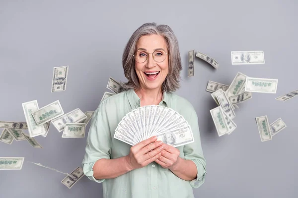 Foto di bella felice eccitato buon umore donna matura tenere soldi vincere lotteria isolato su sfondo di colore grigio — Foto Stock