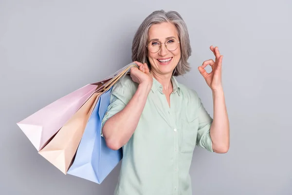 Foto von glücklich positiven lächelnden reifen Frau Shopaholic zeigt Daumen nach oben wie isoliert auf grauem Hintergrund — Stockfoto