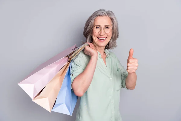 Foto av glada glada leende glad kvinna visar tummen upp hålla shoppingväskor isolerade på grå färg bakgrund — Stockfoto