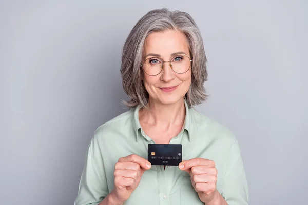 Foto de feliz encantadora avó encantadora em óculos mostrar segurar recomendação de cartão de crédito isolado no fundo de cor cinza — Fotografia de Stock