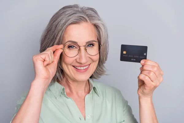Close-up retrato de atraente alegre mulher de cabelos grisalhos segurando lucro cartão bancário isolado sobre fundo de cor pastel cinza — Fotografia de Stock