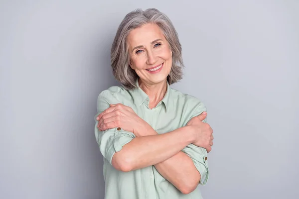 Portrait of attractive cheerful gray-haired woman hugging herself isolated over grey pastel color background