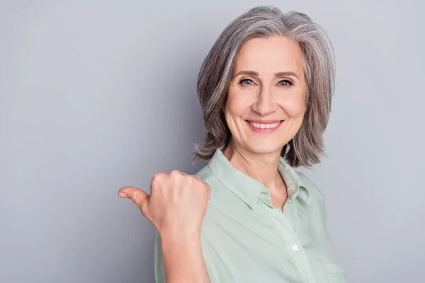 Foto van gelukkig glimlachen mooi volwassen vrouw punt duim copyspace reclame geïsoleerd op grijze kleur achtergrond — Stockfoto