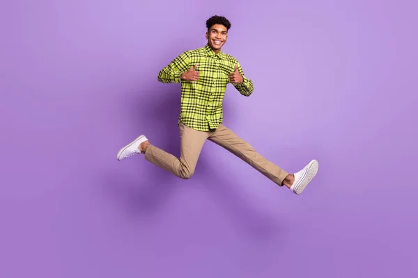 Bilde i full størrelse av mørkhudet brunette - mannen hopper opp, viser tomler opp, går i vanlige klær isolert på fiolett bakgrunn. – stockfoto