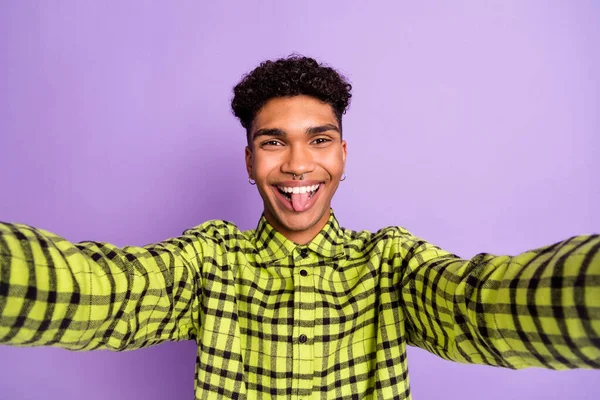 迷人有趣的年轻深色皮肤男人伸出舌头的照片，使自拍相机在紫罗兰的背景下被隔离 — 图库照片
